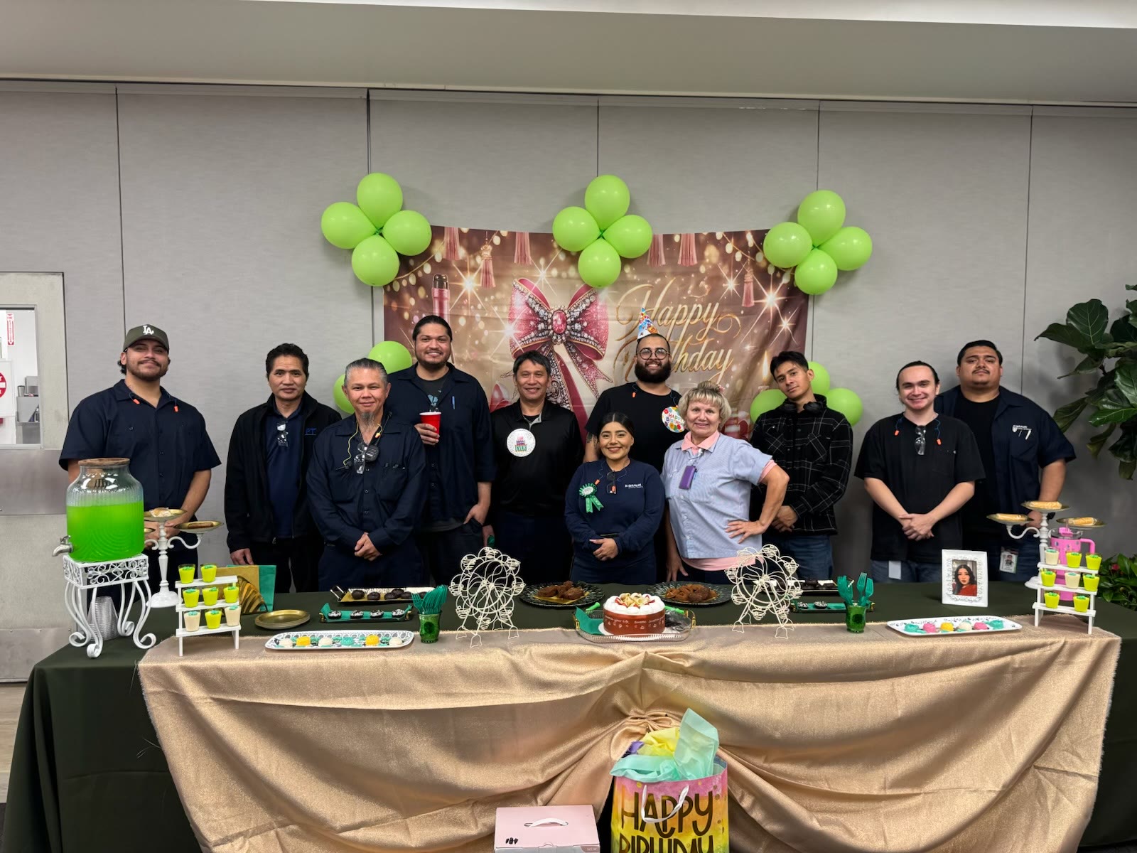 Work crew gathered behind a catered spread with green balloons