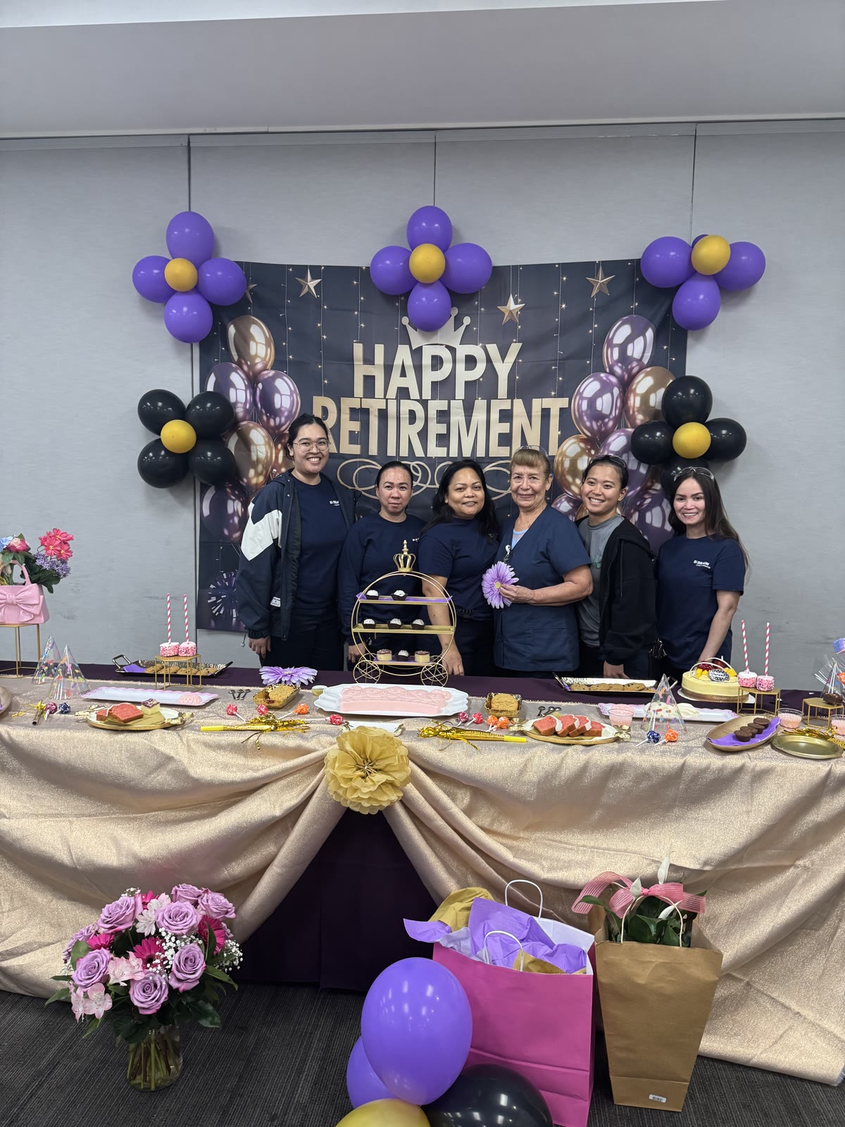 Four coworkers posing at a Happy Retirement dessert table