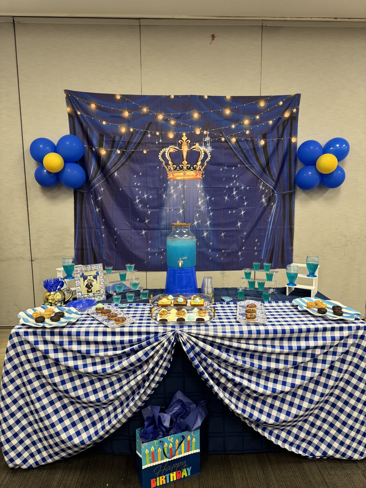 Dessert table styled in royal blue with balloons and a crown backdrop